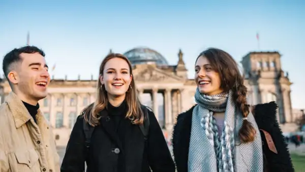 En grupp om tre personer pratar glatt framför Riksdagshuset i Berlin - efter kurs i tyska