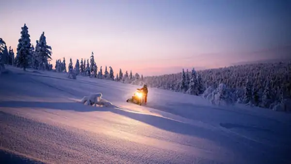 Snöskoter i ett vintrigt finskt landskap vid solnedgång - gå en kurs i finska!