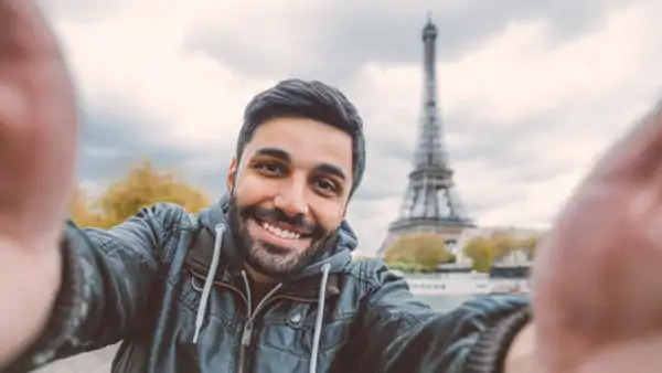 Leende man tar en selfie framför Eiffeltornet i Paris under en kurs i franska